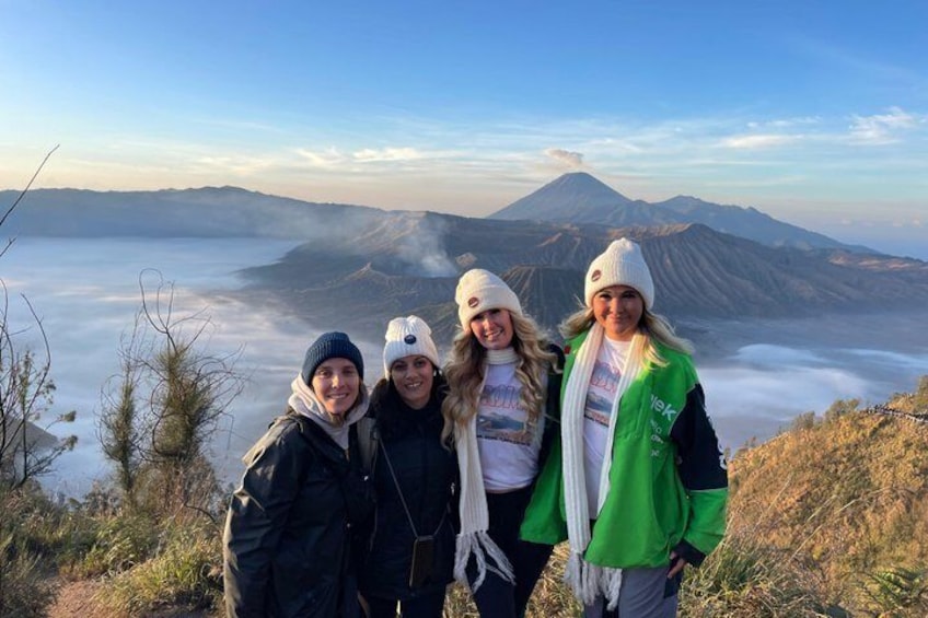 A group of people on a mountain with a view of a volcano and clouds below. 2