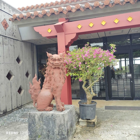 Una estatua de león de terracota, un árbol con flores en maceta y un edificio con tejado de baldosas y entrada roja. 3