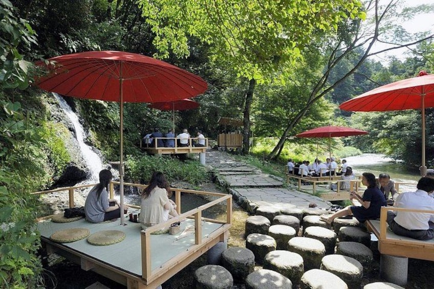 A riverside seating area with red umbrellas, stone steps, and people relaxing. 2