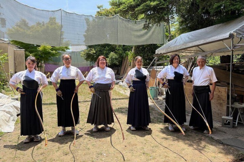 A group of people in traditional attire standing outdoors with a tent and trees in the background. 3