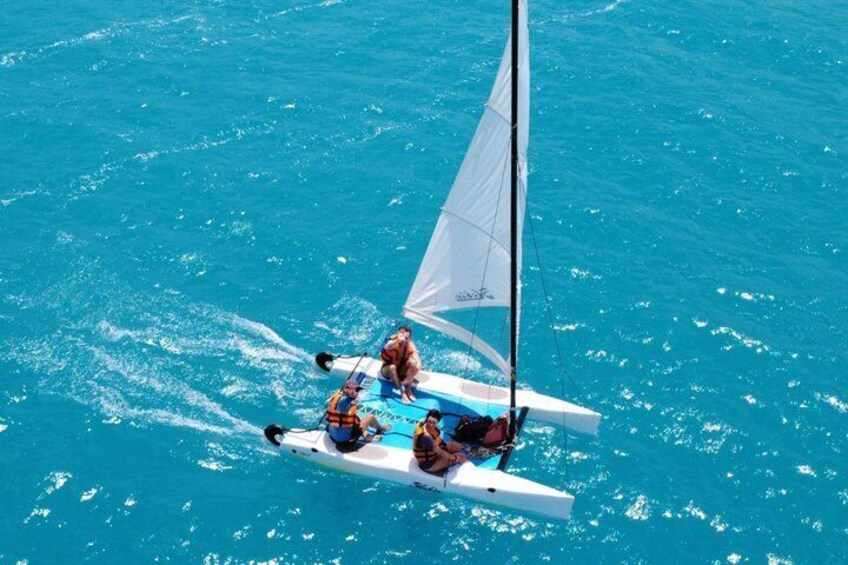 A sailboat with three people on a turquoise sea. 2