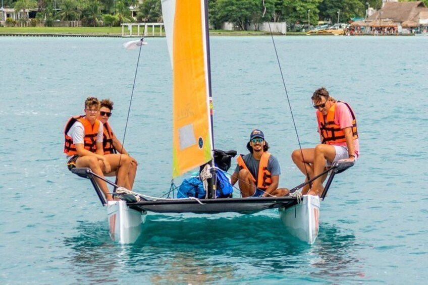 A small sailboat with four people wearing life jackets, anchored in calm water with a clear sky. 3