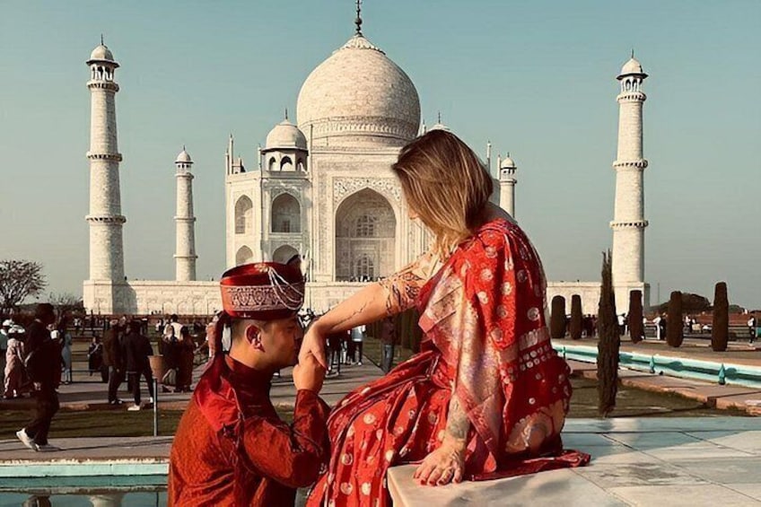 A person in red attire sitting on a marble surface with the Taj Mahal in the background. 1