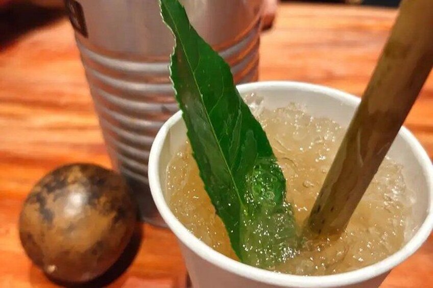 Un bicchiere di tè freddo con una foglia verde e un cucchiaio di legno, un frutto marrone e una tazza a righe sullo sfondo. 4