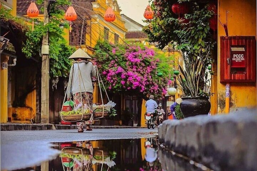 A traditional market scene with a vendor in a conical hat carrying baskets, a street with a waterway, and buildings with traditional architecture. 5