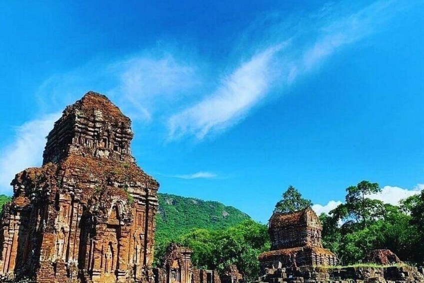 Ancient stone structures with intricate carvings, set against a backdrop of lush green hills and a clear blue sky. 1