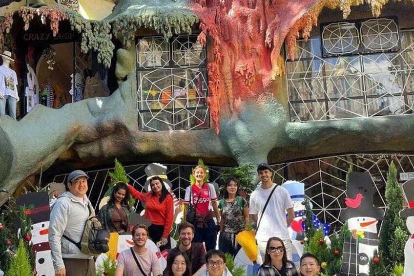 A group of people in front of a whimsical building with a large hand structure and a shop named 'Crazy Shop' in the background. 5
