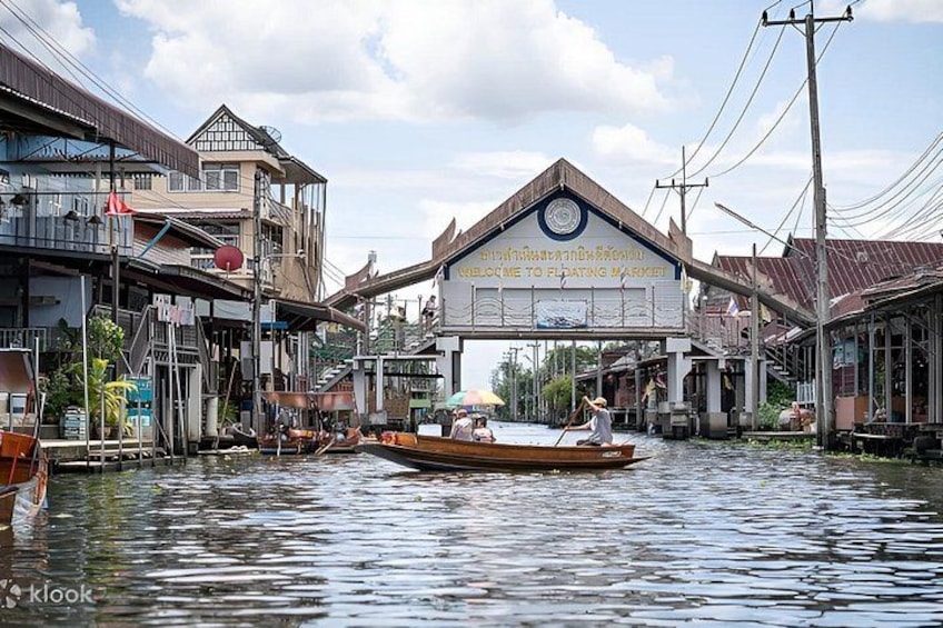 A traditional floating market with wooden boats, a signboard, and buildings along the water. 3