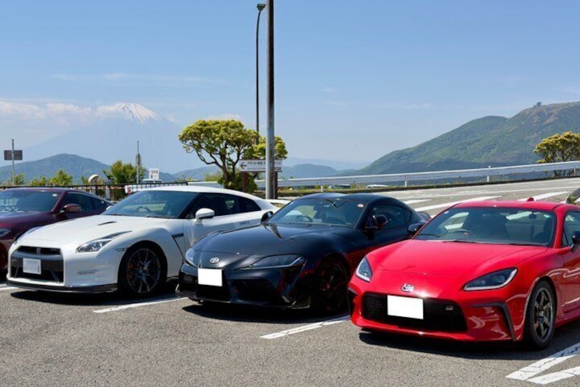 Three sports cars parked on a road with a mountainous landscape in the background. 4