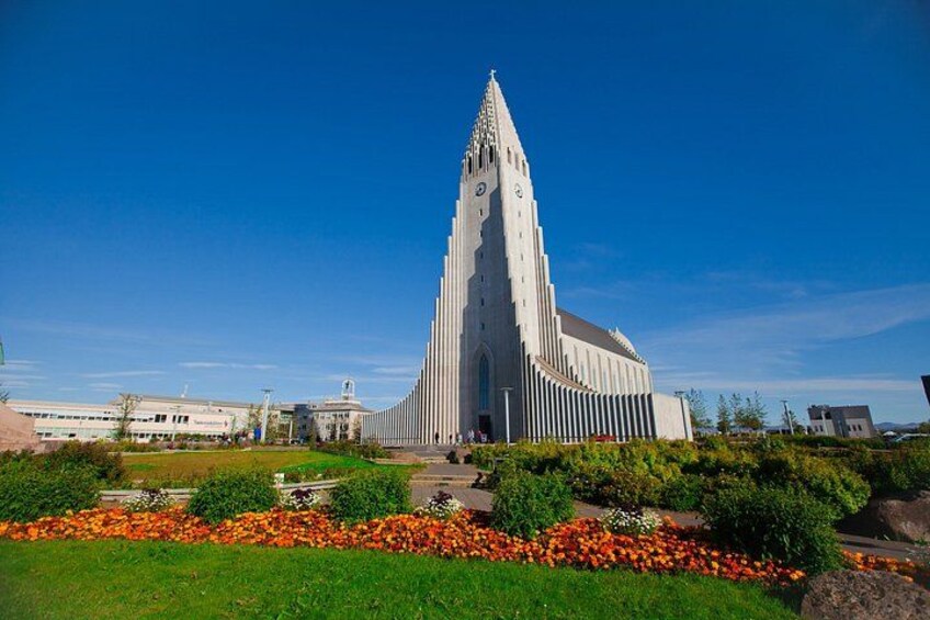 A tall, white church with a pointed spire, surrounded by a well-maintained garden with orange flowers. 2