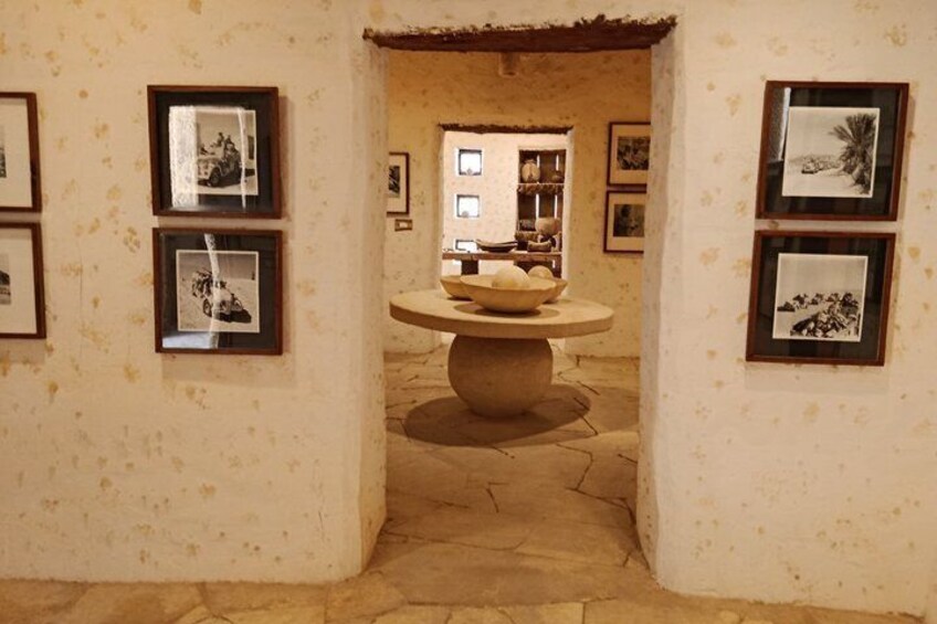 A corridor with framed photographs on the walls, a central stone table with a bowl, and a rustic ceiling. 2