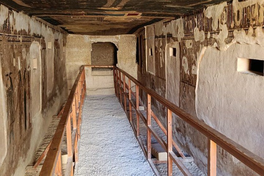 A narrow, dimly lit corridor with a wooden railing, rough walls, and a concrete floor. 2