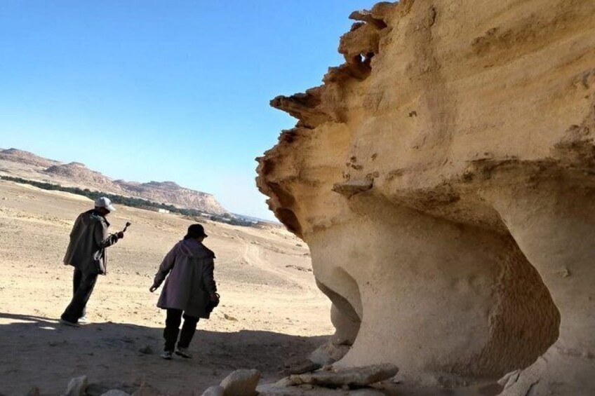 Two people walking in a desert landscape with a large rock formation. 3