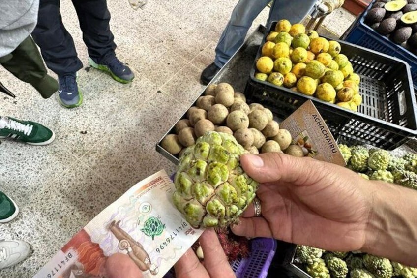 A person holding a fruit and a banknote at a market. 5