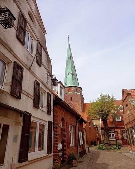A historic street with traditional buildings, a church spire, and a cobblestone path. 1