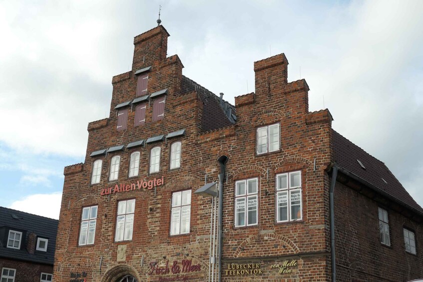 A historic brick building with multiple windows and signs, including 'Zur Alten Vogtei' and 'Lübecker Teekontor.' 2
