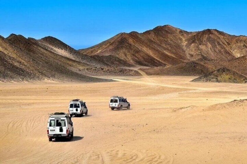 Three off-road vehicles on a desert road with mountains in the background. 2