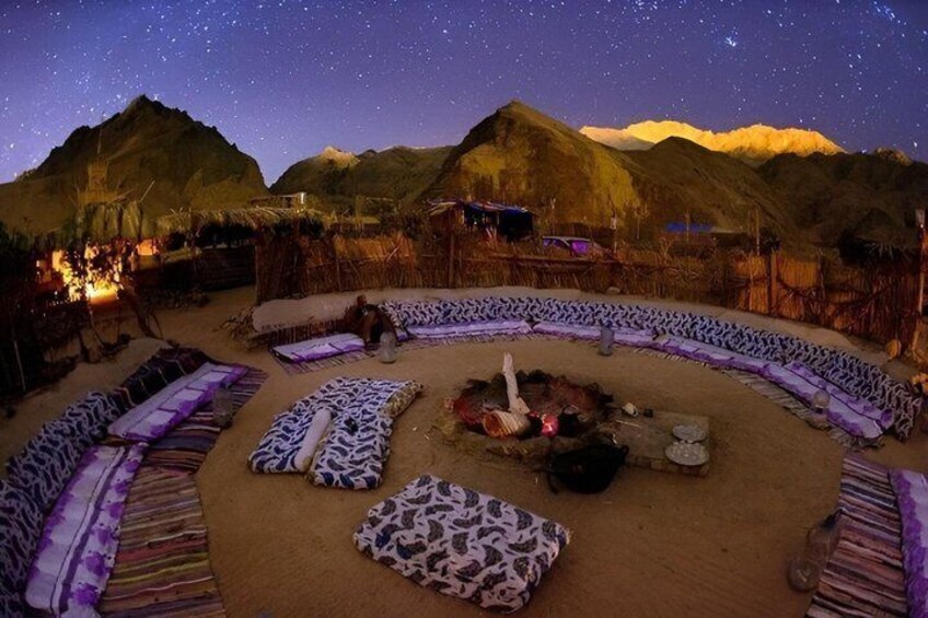 A starlit desert scene with a fire pit and patterned cushions. 2