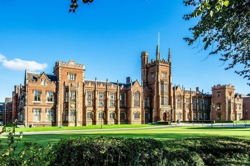 A large, historic brick building with multiple towers and a well-maintained lawn. 3
