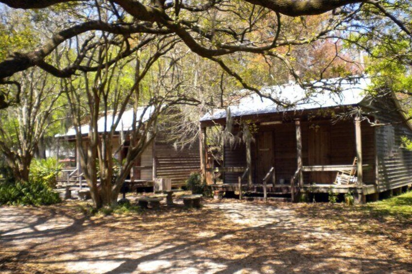 A rustic cabin with a porch, surrounded by trees and a wooden fence. 2