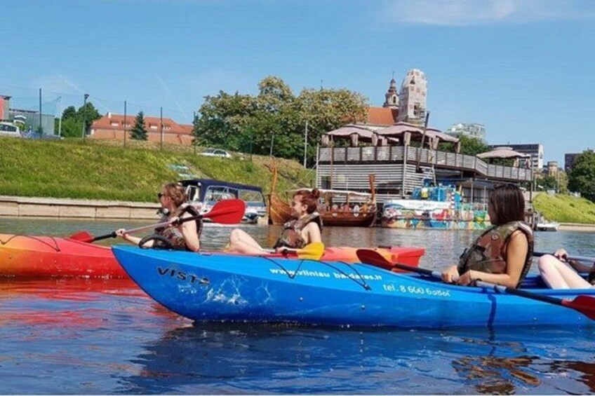 A group of people kayaking on a river with a bridge and buildings in the background. 5
