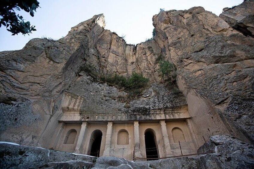 A rock-cut tomb with three arched doorways and a central niche, set against a rugged cliff face. 3