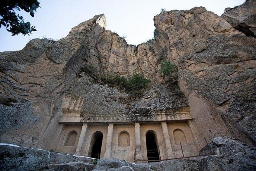 A rock formation with carved niches and a cave entrance. 3