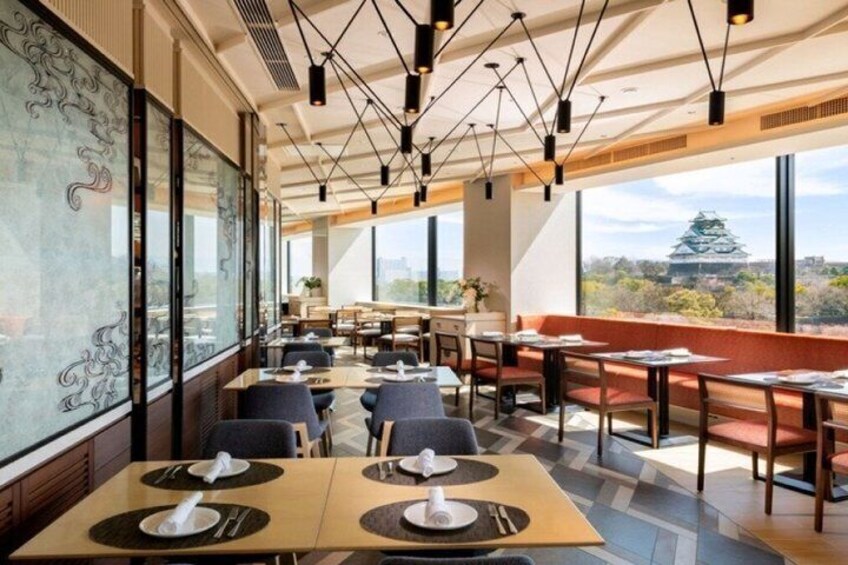 A restaurant with tables set for dining, large windows, and a view of a castle. 4