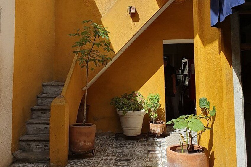 A yellow building with a staircase, potted plants, and a tiled floor. 2