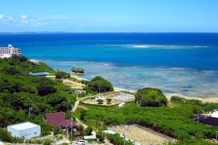 A coastal landscape with a clear view of the ocean, a beach, and a building surrounded by greenery. 1