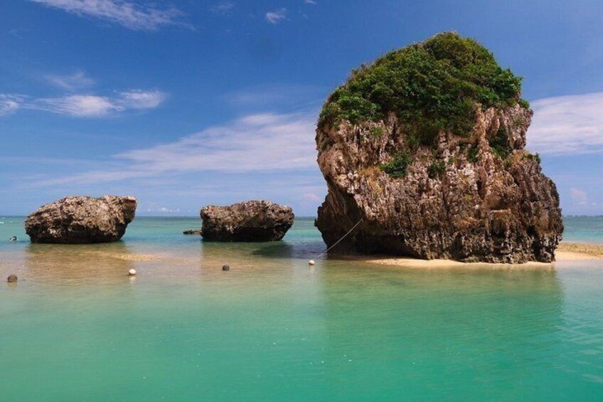 A clear turquoise sea with three rocky formations, one with vegetation. 4