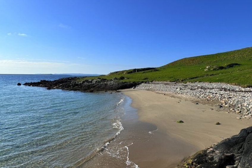 A sandy beach with gentle waves, a rocky shoreline, and green hills in the background. 3