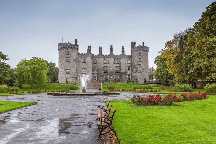 A castle with a fountain, lush green lawn, and red flowers. 2