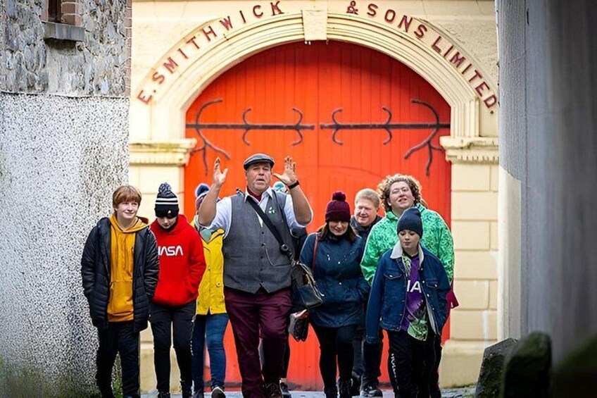 A group of people standing in front of a red door with the inscription 'E. SMITHWICK & SONS LIMITED.' 2