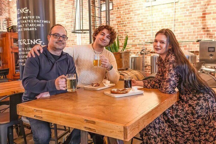 Three people sitting at a wooden table in a brick-walled cafe, holding mugs. 2