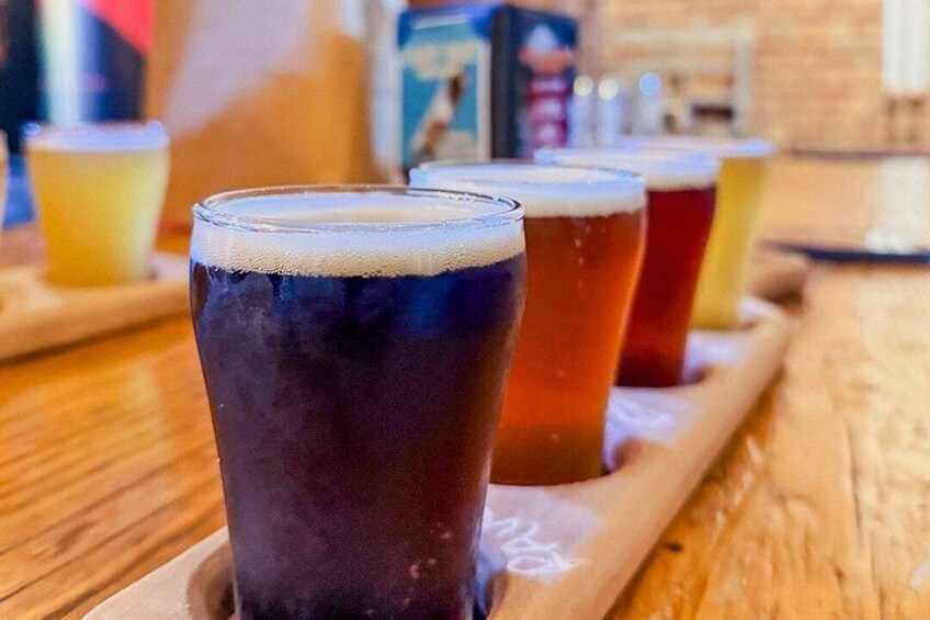 A wooden tray with four glasses of beer, one dark and three lighter shades. 4
