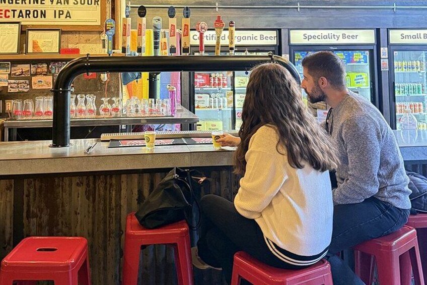 A bar with a counter and stools, a beer tap, and refrigerated shelves with various beverages. 3