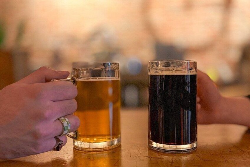 Two hands holding beer mugs, one with a light beer and the other with a dark beer, on a wooden table. 5