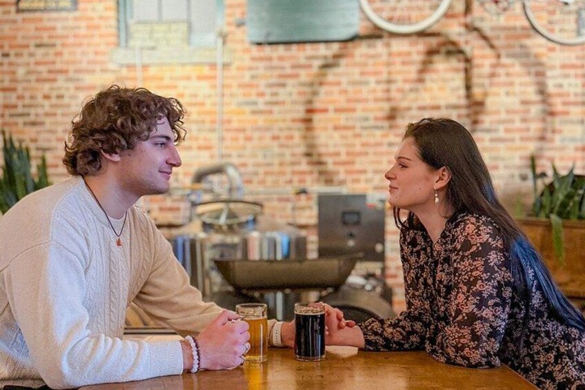 Two people sitting at a table with a beer mug in front of them. 1