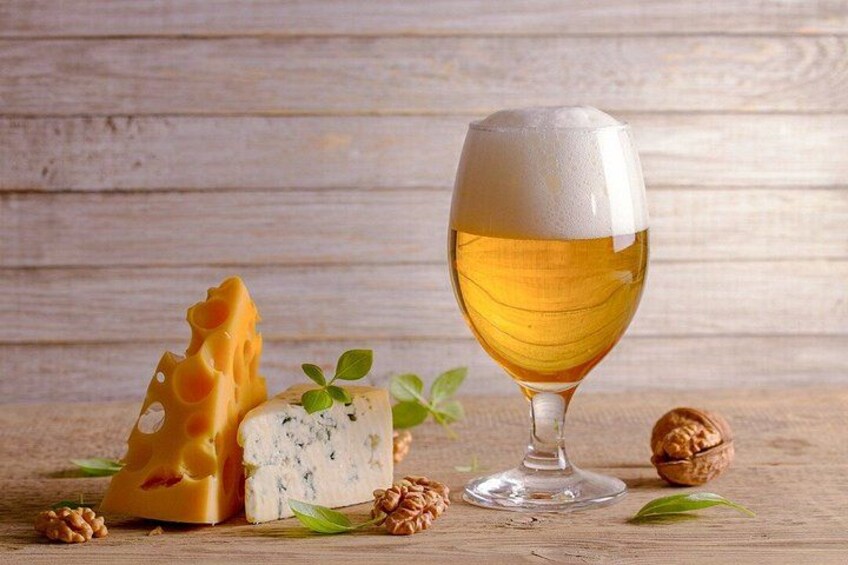 A glass of beer, a wedge of cheese, a piece of blue cheese, walnuts, and a basil leaf on a wooden surface. 2