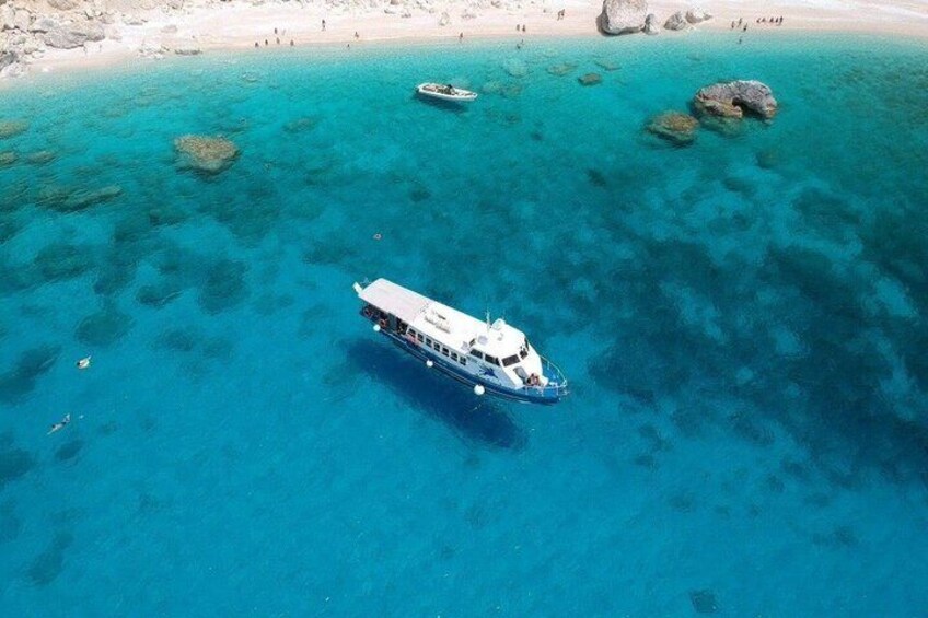 A boat on clear turquoise waters with a beach and rocks in the background. 1