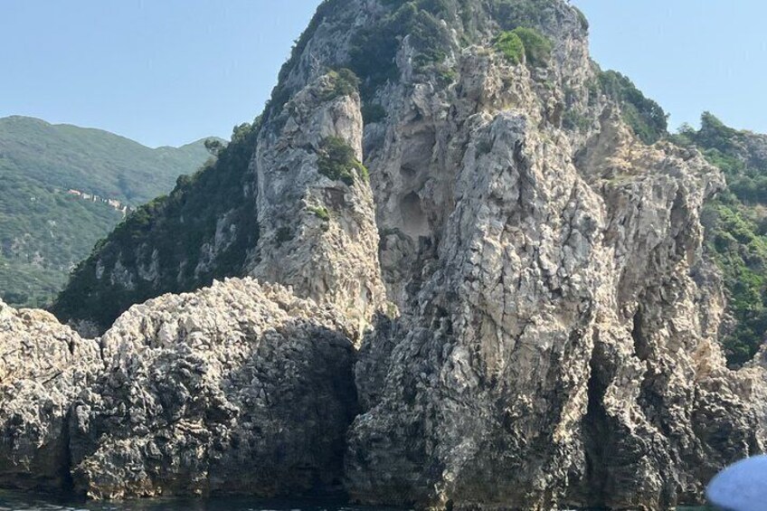 A rugged cliff with a cave entrance, surrounded by greenery and hills. 3