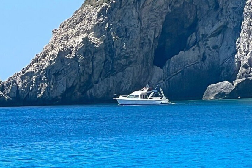 A boat on a calm sea with a rocky cliff in the background. 5