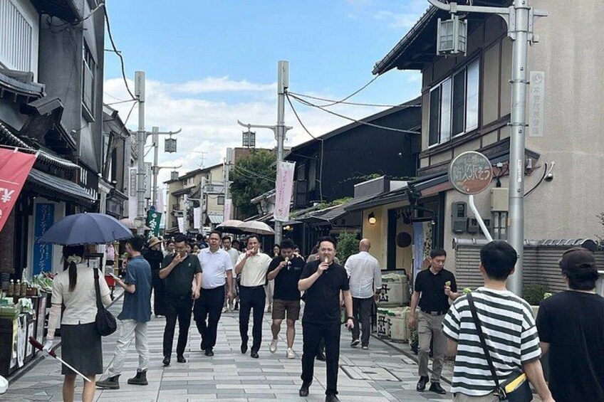 A crowded street with people walking and standing, buildings lining the street, and a clear sky. 3