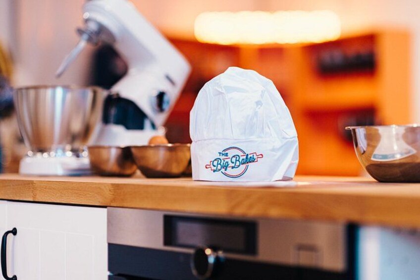 A kitchen countertop with a stand mixer, mixing bowls, and a white plastic bag with 'The Big Bakes' logo. 2
