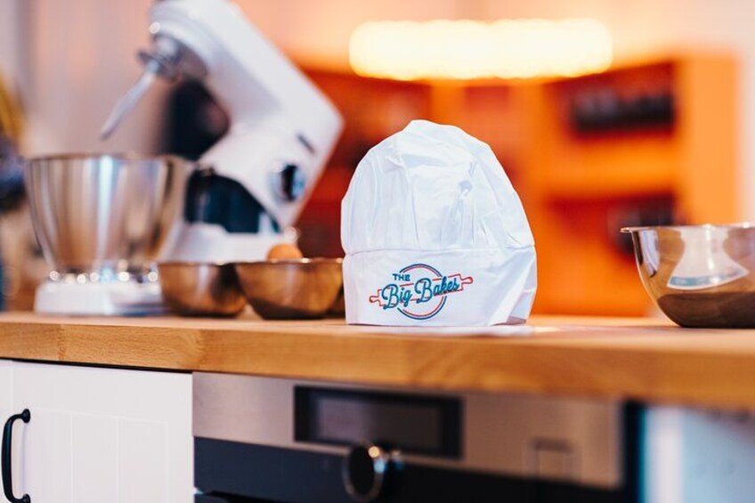 A kitchen countertop with a stand mixer, mixing bowls, and a white plastic bag with 'The Big Bakers' logo. 3