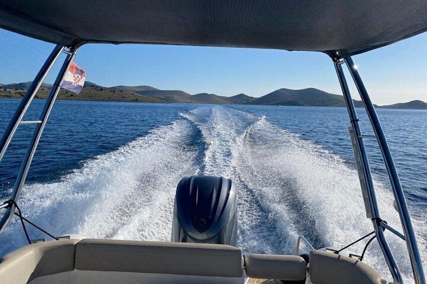 A boat moving through water with wake behind it, a flag on the left, and distant land. 5