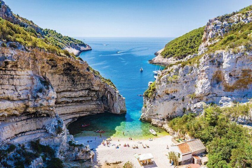 A coastal landscape with cliffs, a clear blue sea, and a beach with people and boats. 3
