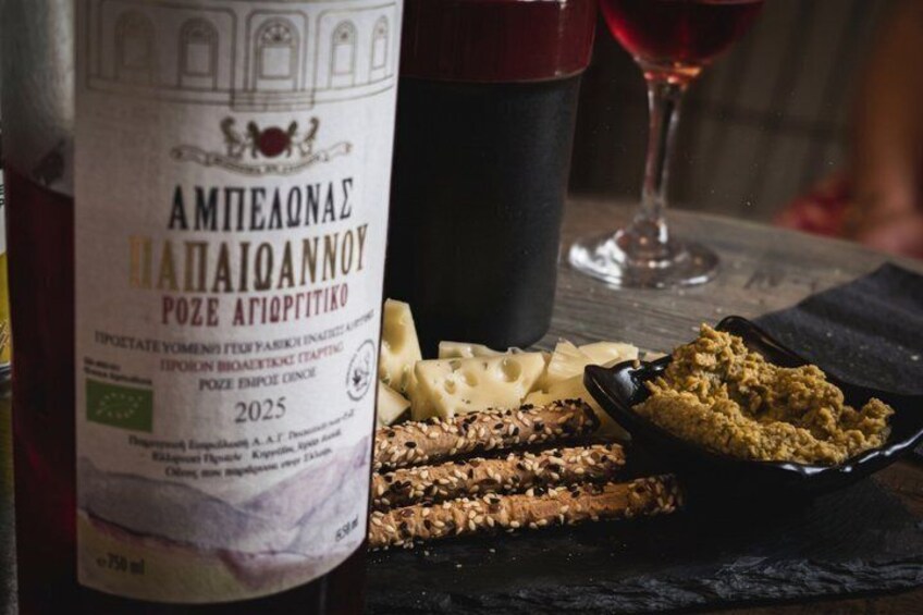 A bottle of wine, a glass of red wine, cheese, crackers, and a bowl of nuts on a table. 3