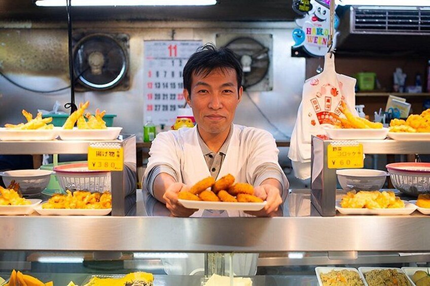 A person serving food at a counter with various dishes and a calendar in the background. 1